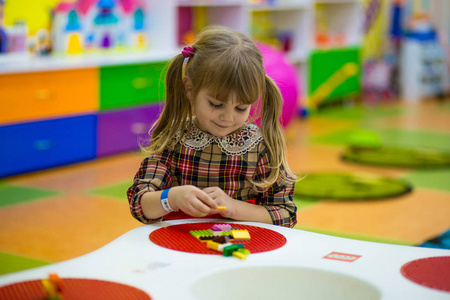 快乐微笑的小女孩在儿童室内逻辑游戏立方马赛克中玩彩色构造器。 由立方体创建的设计。 逻辑思维几何形状的概念。