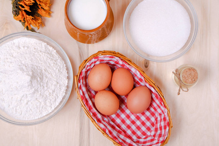 柳条鸡蛋，一堆面粉，一杯牛奶，黄油，放在白色的木桌上烤