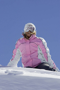 白种人女子滑雪者穿着冬季服装坐在山腰上