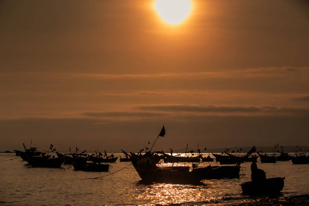 越南渔船在海面上的剪影，映衬着明亮的晚霞倒影和巨大的太阳盘