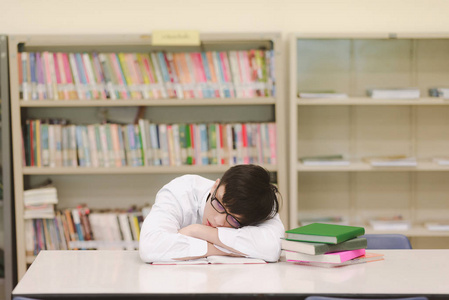 年轻的学生在图书馆努力学习。 亚洲男大学生在图书馆做学习研究，睡着与书籍和桌子和微笑。 回到学校的教育理念。