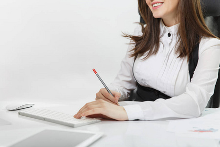 微笑棕色头发业务妇女在西装和眼镜坐在办公桌, 在计算机与现代显示器与文件在轻型办公室, 看着在白色背景的摄像头关闭