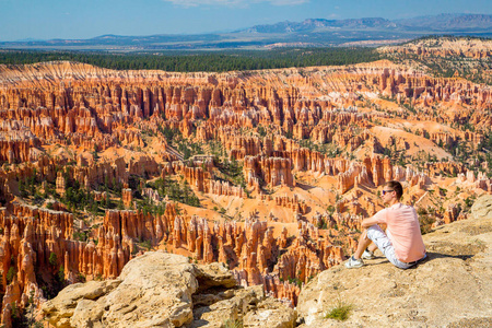 在美国犹他州布莱斯峡谷国家公园，坐在风景秀丽的红砂岩头罩旁边的年轻人