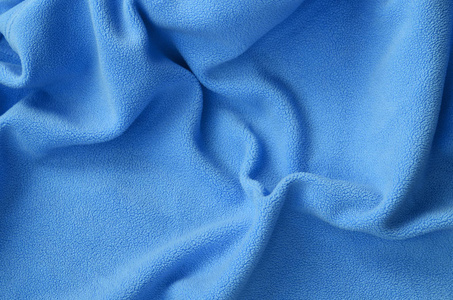 毛茸茸的蓝色羊毛织物的毯子。 背景浅蓝色软毛绒材料，有很多浮雕褶皱