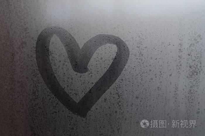 爱的心形手画在潮湿冻结的窗户窗格与早晨的阳光背景.