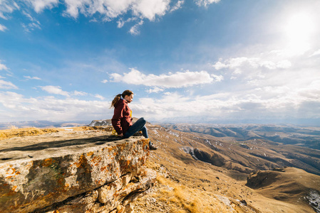 活跃的年轻女孩坐在悬崖边上, 享受着高山的空气和阳光