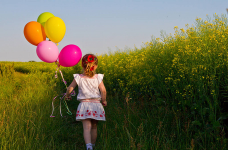 穿着裙子的小亚洲女孩手里拿着气球跑过绿色的麦田，慢动作