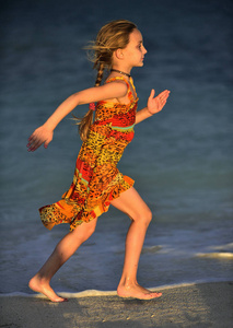 可爱的小女孩在夕阳下在海滩上奔跑。 古巴。