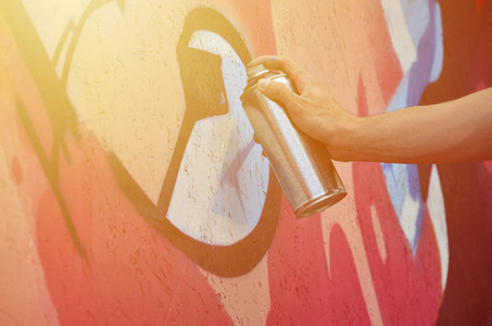 一只手带着喷雾器，在墙上画了一个新的涂鸦。 在木墙上画涂鸦的过程的照片。 街头艺术和非法破坏的概念