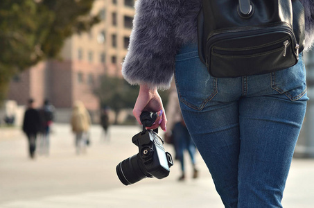 一位女摄影师的后景，手里拿着现代单反相机，对着一条模糊拥挤的街道