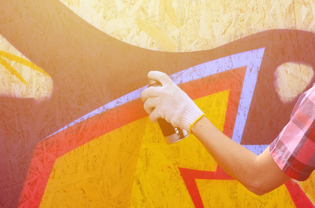 一只手带着喷雾罐，在墙上画了一个新的涂鸦。木墙特写画涂鸦的过程照片..街头艺术和非法破坏的概念
