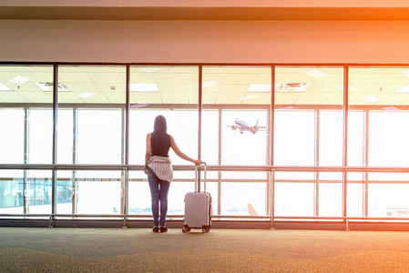 旅客妇女计划和背包看到飞机在机场玻璃窗女孩游客拿着包，并在大厅飞机起飞的行李附近等待。 旅行概念。