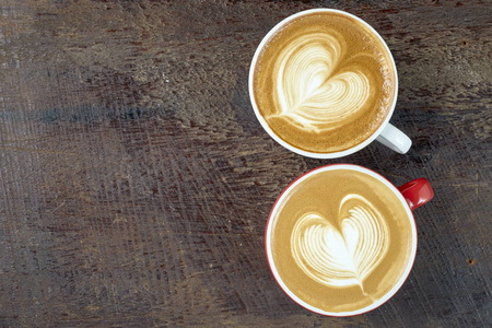 木制桌子上的咖啡杯中的两个咖啡或拿铁艺术心形