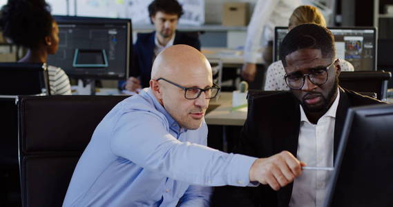 年轻的非洲裔美国办公室工作人员的肖像咨询他的老板关于他们的商业项目策略在计算机上。城市办公室与工作者在模糊的背景。室内