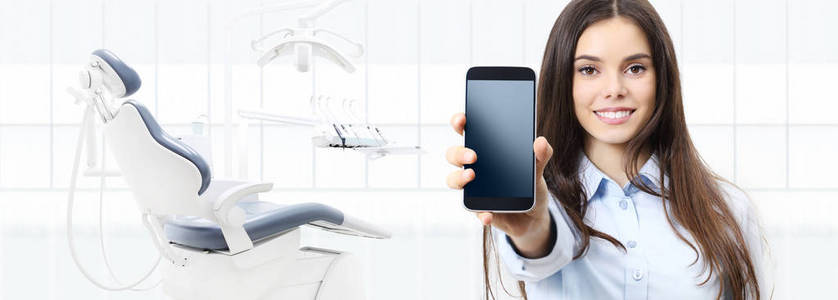 牙科保健微笑的妇女显示智能手机在牙医诊所
