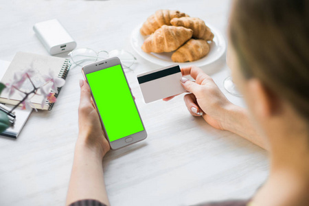 智能手机和信用卡借记卡在手的女孩智能手机绿色屏幕的色度键。互联网商务和网上购物的商品和服务支付