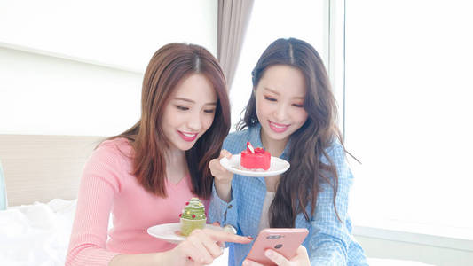 两位美女高兴地自拍，在床上吃蛋糕