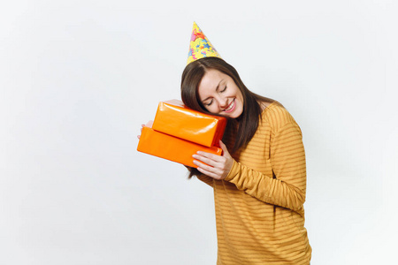 美丽的白种人有趣的年轻快乐的女人在黄色的衣服, 生日派对帽拿着礼物的橙色礼品盒, 庆祝和享受在白色背景的广告隔离的节日