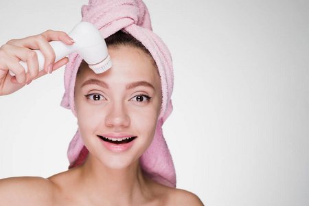 可爱的年轻女孩用毛巾在脸上用特殊的电刷进行深层洁肤