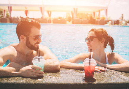 在游泳池边的一对年轻夫妇。男人和女人在水里喝鸡尾酒