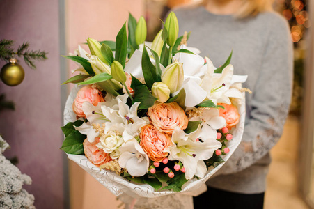 雌性拿着花束百合花, 兰花, 在白色包装纸的钢琴形状的玫瑰