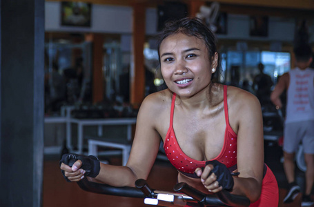 年轻美丽的出汗亚洲快乐的女人训练微笑硬骑车和骑在健身房运动健身身体护理静态自行车锻炼