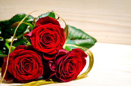 三朵美丽的红玫瑰被包裹在一条金色的丝带里，它有一个心形。