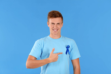 青年男子指着他的 tshirt 与色彩背景蓝色丝带。前列腺癌认知概念