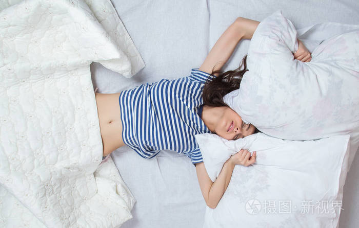 照片 年轻漂亮的女人在灯光室醒来. 放松的女人躺在床上穿着睡衣.