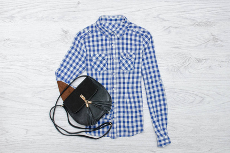 蓝色和白色格子衬衫和黑色手提包。木制背景