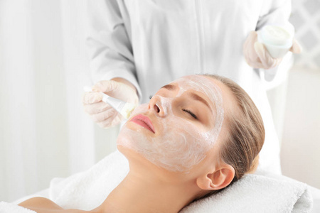 美容师在 spa 沙龙的年轻女子脸上涂抹面膜