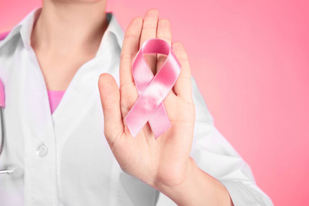 医生在颜色背景上显示粉红色缎带。乳癌意识概念
