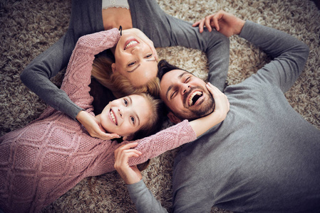 幸福的年轻家庭的顶部景色微笑着躺在地板上的相机。
