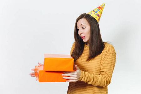 美丽的白种人有趣的年轻快乐的女人在黄色的衣服, 生日派对帽拿着礼物的橙色礼品盒, 庆祝和享受在白色背景的广告隔离的节日