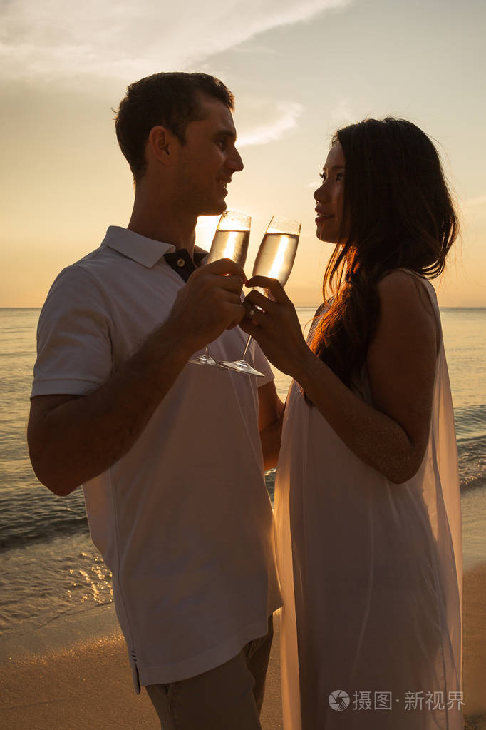 在热带岛屿的夕阳下,浪漫的情侣在海滩上相爱.互相看着对方.