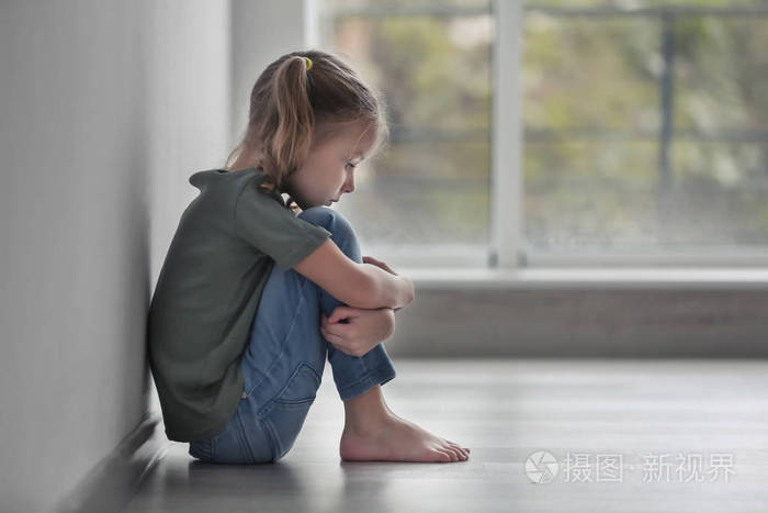 伤心的小女孩坐在室内的地板上