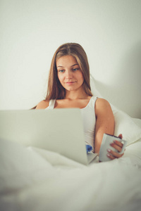 一个年轻的女人在床上，享受一杯茶的笔记本电脑