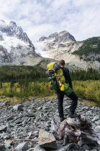 一个冒险的年轻人穿着一个沉重的背包站在原木上，欣赏着群山环绕的美丽景色。 远离温哥华和西雅图华盛顿美国东部。