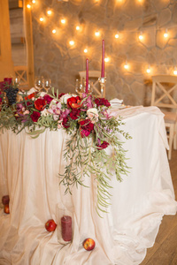 婚礼桌上的一套酒色蜡烛，周围是淡淡的花环和鲜花。内政。复制空间