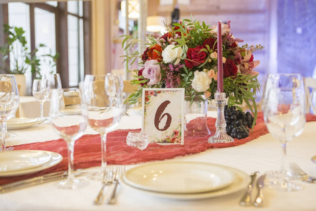 婚礼桌上的一套玻璃和盘子，周围是浅色的花环和葡萄酒颜色的花和桌布。内政。复制空间