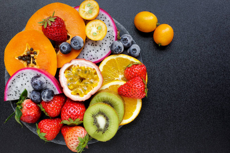 一碗健康沙拉，从新鲜水果在黑暗的桌子上。 混合新鲜水果草莓橙蓝莓猕猴桃西番莲。从上面可以看到健康的素食午餐碗。