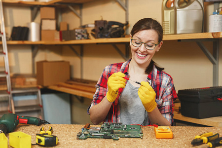 电工用万用表。漂亮的年轻女子在黄色手套, 眼镜数字电子工程师维修, 焊接计算机 Pc 主板在车间在不同的工具木桌
