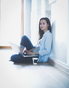 年轻漂亮的女人在家里坐在用笔记本电脑在地板上。年轻漂亮的女人