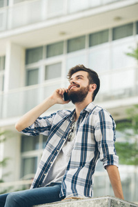 英俊的大胡子男人坐在户外用手机聊天