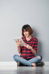 漂亮的亚洲年轻女子坐在地板上，在平板电脑上看书
