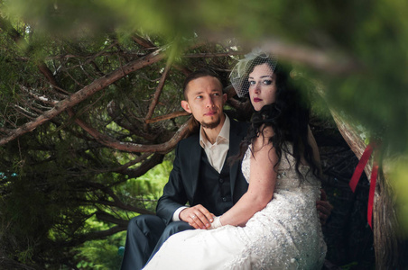 黑发新娘妻子和她未婚夫在一个绿色的秋天公园散步。 她穿着一件带有花束的复古长裙，穿着刺的脸藏在面纱下