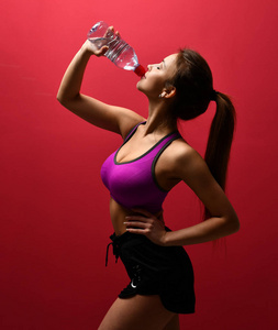 年轻俏丽的妇女饮用的水在紫色运动胸罩