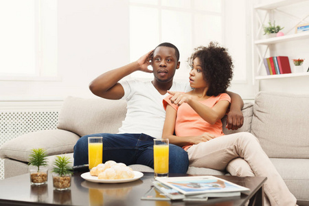 惊讶的非洲裔美国年轻夫妇在家看电视