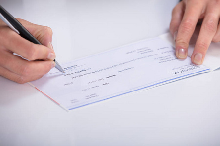 s Hand Signing Cheque On Desk In Office