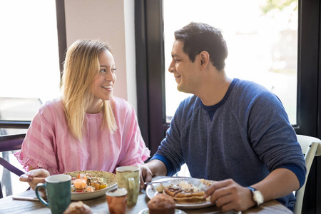一对漂亮的年轻夫妇在餐馆约会时互相看着，微笑着